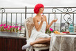 beautiful young female with red hair in a white towel eats at a table on the terrace