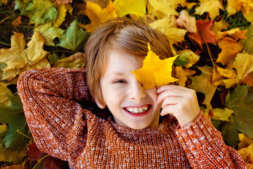 autumn children. a boy in an autumn park lies on the ground and covers one eye with a maple leaf. a 