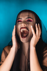 Evil bride with black makeup and veil laughing on blue