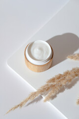 Wall Mural - natural organic moisturizer cream in eco friendly bamboo jar and dried flowers on white podium. eco 