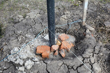 A Close-up On A Fence Metal Post Installation, Setting In Concrete Using A Level Line Or String, Crashed Gravel, Broken Bricks And Concrete To Fill The Post Hole.