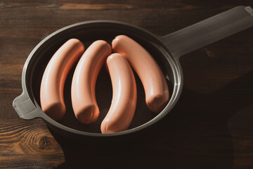 Fototapete - Toy sausages on a frying pan on a wooden background. Plastic toy