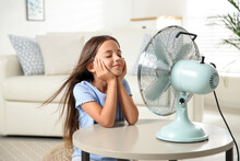 Little Girl Enjoying Air Flow From Fan At Home. Summer Heat