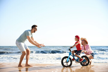 Sticker - Happy parents teaching son to ride bicycle on sandy beach near sea