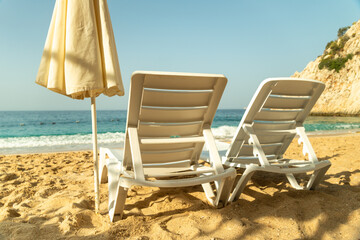 Wall Mural - Empty Beach chairs and a yellow sun umbrella await tourists against the backdrop of the blue sea and beautiful ocean waves and blue sky. Beautiful seashore beach resort.