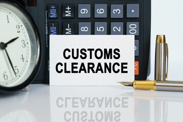 On the table there is a clock, a pen, a calculator and a business card on which the text is written - CUSTOMS CLEARANCE