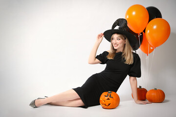 Wall Mural - Beautiful woman in witch costume with balloons and pumpkins on white background, space for text. Halloween party