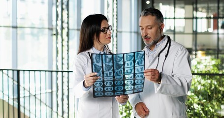 Wall Mural - Caucasian couple of male and female doctors standing in hospital, talking and looking at X-ray. Professionals man and woman, physicians discussing work and watching on diagnosis. Docs.