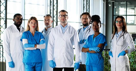 Wall Mural - Portrait of multi ethnic women and men, team of doctors colleagues. International medics. Healthcare workers. Mixed-races physicians and nurses looking at camera. Clinic team. Docs at work in hospital