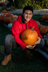 teen boy in red sweatshirt and jeans at pumpkin patch holding a pumpkin and smiling at camera