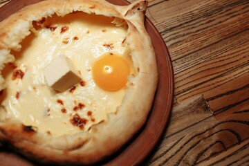 Top view on traditional Adjarian Khachapuri - open baked pie with melted salt cheese suluguni and egg yolk on wooden tray. Traditional georgian food