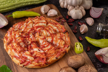 Pizza on a wooden tray with bell peppers, garlic, chili, shiitake mushrooms, and a jar of pepper seeds.