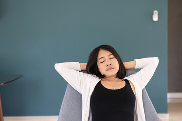 Wall Mural - Asian woman sitting on couch in living room with hands over head,Relaxing time