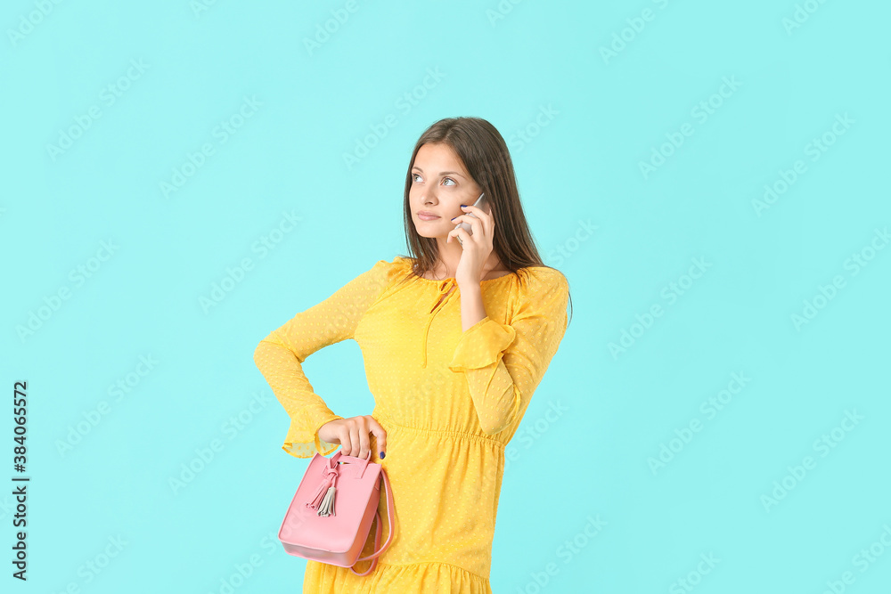 Beautiful young woman talking by phone on color background