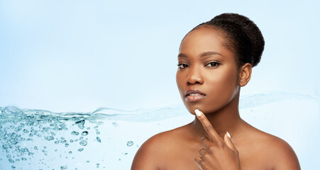 beauty and people concept - portrait of young african american woman with bare shoulders touching her chin over blue background with bubbles in water splash