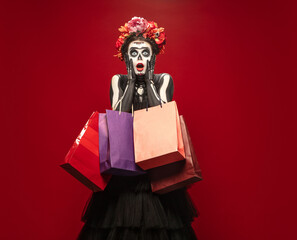 Shopping. Young girl like Santa Muerte Saint death or Sugar skull with bright make-up. Portrait isolated on red studio background with copyspace. Celebrating Halloween or Day of the dead. Black friday