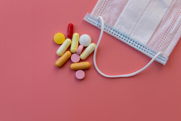 medical mask and pills, pills scattered on pink background close-up with copy space