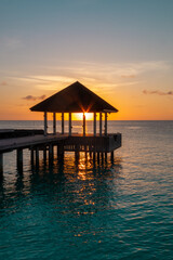 Sun light goes through building on water of Indian ocean during sun set on Maldive islands