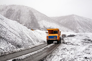 Wall Mural - A mining dump truck drives on a dirt road in a mountainous area. It's still autumn, but already there is a snow cover around