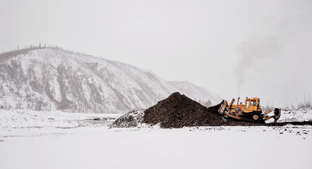 Wall Mural - A bulldozer in a mountainous area in an industrial area shovels up a pile of mountain soil. Mining.