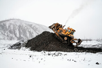 Wall Mural - A bulldozer in a mountainous area in an industrial area shovels up a pile of mountain soil. Mining.