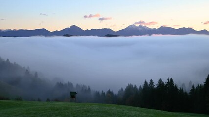 Wall Mural - Time lapse low inversion clouds rolling in Alpine valley, Slovenia. Fog covers the landscape. Alps mountains range in the distance. Static shot, wide angle