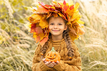 Wall Mural - A little girl with an autumn wreath on her head and a pumpkin in her hands.