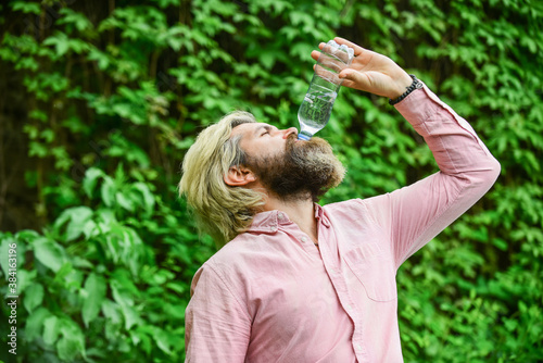 To the dregs. feeling thirsty. drink some water while walking in park. get refreshed. Maintain water balance in the body. brutal male hipster drink water. bearded man hold plastic bottle of water