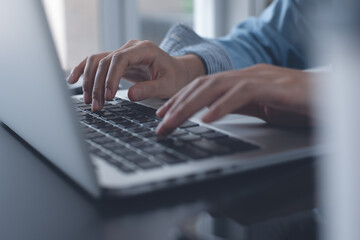 close up of woman hands typing on laptop computer keyboard on wooden table