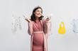 © LIGHTFIELD STUDIOS - joyful pregnant woman holding tiny boots near baby clothes on clothing line isolated on white