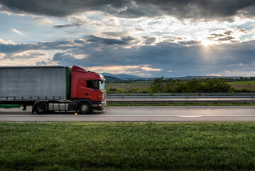 Wall Mural - Red truck is on highway - business, commercial, cargo transportation concept, beautiful sunset sky, clear and blank space - side view