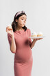 © LIGHTFIELD STUDIOS - young pregnant woman holding plate while eating cupcake isolated on white