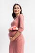 © LIGHTFIELD STUDIOS - pleased pregnant woman with floral belt standing isolated on white