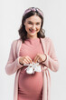 © LIGHTFIELD STUDIOS - joyful and pregnant woman holding tiny baby boots isolated on white