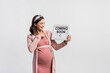 © LIGHTFIELD STUDIOS - joyful pregnant woman pointing with finger at board with coming soon lettering isolated on white