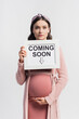 © LIGHTFIELD STUDIOS - pregnant woman holding board with coming soon lettering isolated on white
