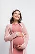 © LIGHTFIELD STUDIOS - pregnant woman in cardigan and headband touching belly isolated on white