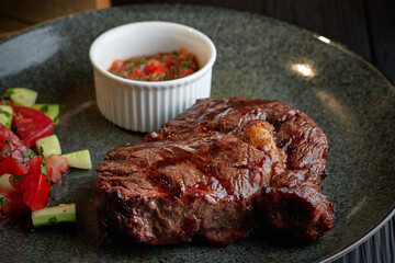 Wall Mural - Meat steak with vegetables and sauce, on a dark plate, on a black background