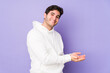 © Asier - Young man isolated on purple background holding a copy space on a palm.