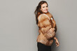 Side view of a model girl in an expensive luxurious fur coat isolated at the grey background. Winter fashion