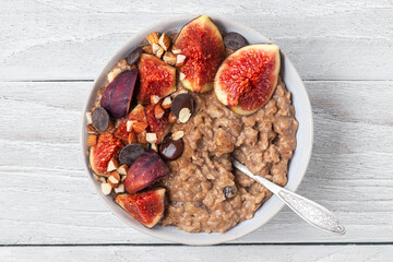 Poster - Oatmeal porridge with figs, cinnamon, chocolate and almonds in a bowl with spoon on white wooden background