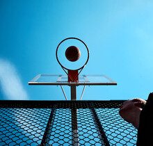 The Basketball Player Scores A Goal. The Basketball Flies Right Into The Center Of The Ring. Sports Equipment On A Background Of Sunny Blue Sky.