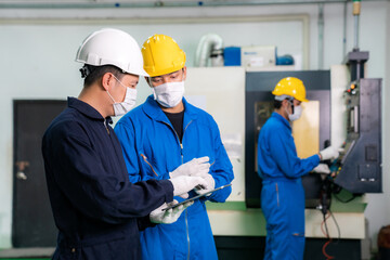 Asian industrial engineers and worker in hard hats discuss product line while using digital tablet and make showing gestures and work in a heavy industry manufacturing factory.