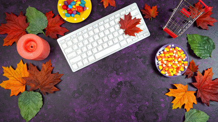Wall Mural - Happy Halloween Trick or Treat theme desktop with candy and lollipops, autumn leaves on stylish purple textured background. Top view blog hero header creative flat lay. Negative copy space.