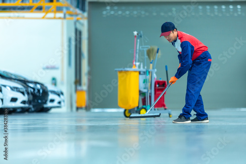 Asian worker in car mechanic repair service center cleaning using mops to roll water from the epoxy floor. Mops in the car repair service center..