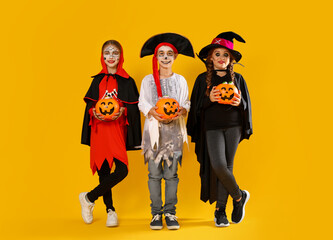 Canvas Print - Cute little kids with pumpkin candy buckets wearing Halloween costumes on yellow background