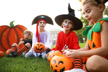 Poster - Cute little kids with pumpkin candy buckets wearing Halloween costumes in park