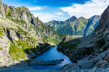 Mountain summer scenery. Shaded lake in the valley by the surrounding rock walls. In the background, the green slopes of the peaks. Tatry Mountains. Slovakia.