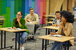 © Friends Stock - Group of young multiracial people sitting at desks in the modern office and listening to coach or speaker during corporate team building training or business seminar