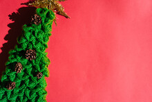 Handmade Green Knitted Christmas Tree With A Gold Tinsel Star On Top And Small Pine Cones. Beautiful Red Gradient Christmas Background And Lots Of Empty Space For Text.